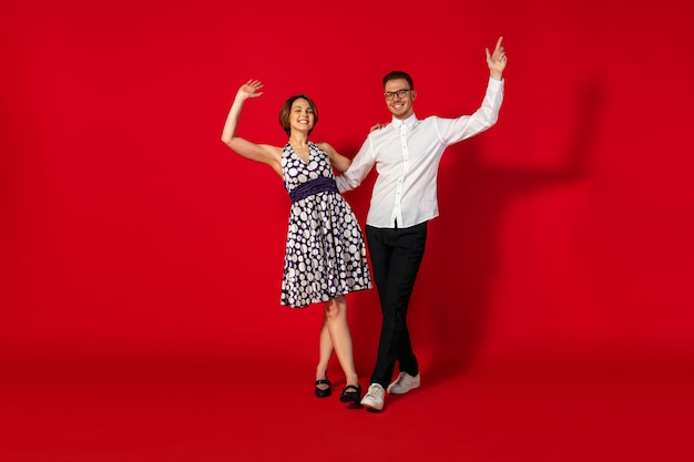 Rock n roll. Old-school fashioned young woman dancing isolated on red studio background. Young stylish man and woman.