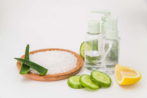 Rock salt on wooden plate; cucumber slices; lemon and spray bottle on white backdrop