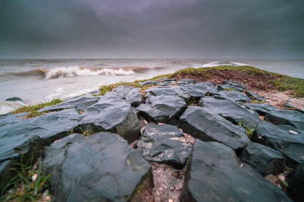 Rocks covered in mosses and surrounded by the wavy sea under a cloudy sky in the evening