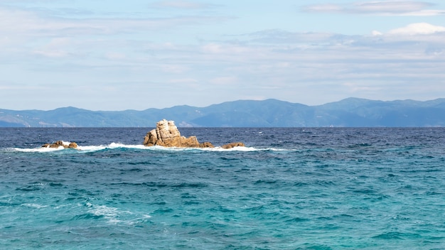 Rocks in the water of the Aegean sea with land in the distance in Greece