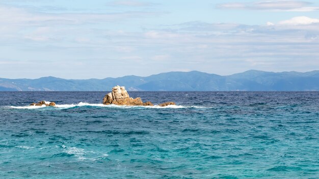 Rocks in the water of the Aegean sea with land in the distance in Greece