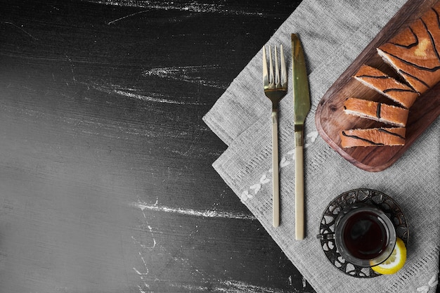 Roll cake slices on a wooden board with a glass of tea, top view.