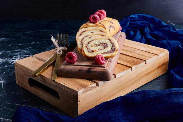 Roll cake with chocolate and berries on a wooden tray. 