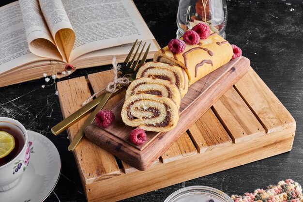 Roll cake with chocolate cream and a cup of tea on a wooden tray. 
