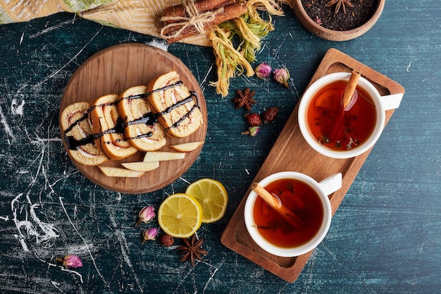 Rollcake slices on a wooden platter with cup of tea.