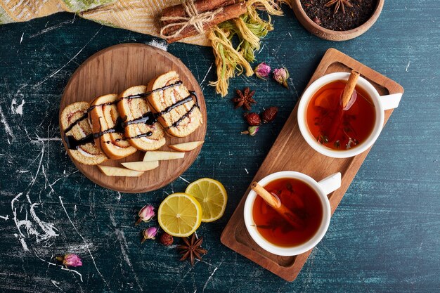 Rollcake slices on a wooden platter with cup of tea.