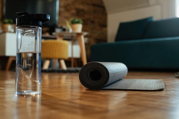 Свернутый коврик для упражнений и бутылка воды на паркетном полу.