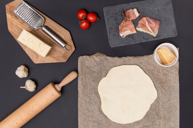 Rolled out pizza dough; pizza ingredient and raw meat with kitchen utensil over kitchen counter