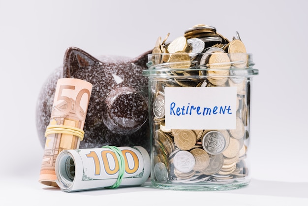 Rolled up banknotes; piggybank and retirement container full of coins on white backdrop