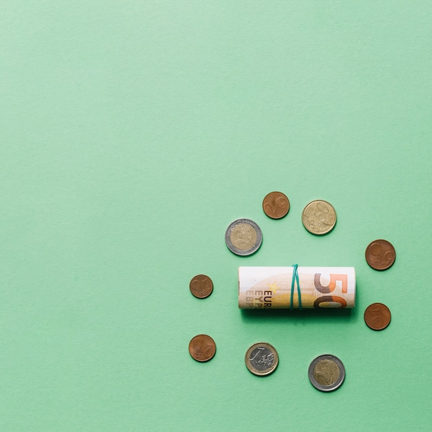 Free photo rolled up euro bank note with coins on green backdrop