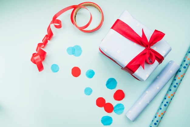 Free photo rolledup gift paper; red ribbon; and present on blue background