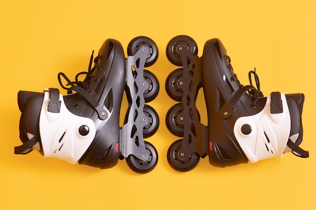 Roller skates isolated on yellow, pair of new cool white and black rolling skates, equipment for active sport training, rinking, roller skating, rollerblading. Active rest concept.