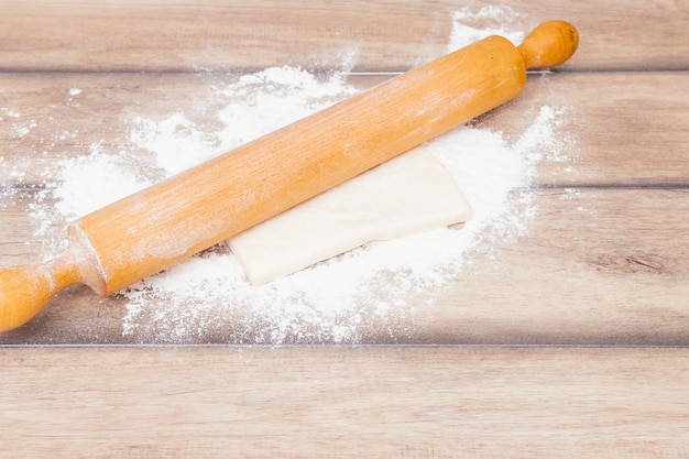 Rolling pin over the kneaded dough and flour on wooden table