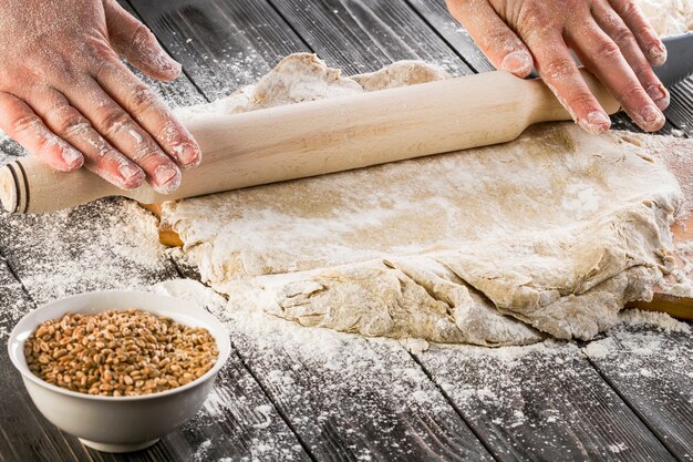 Rolling the wheat dough with flour on the wooden table