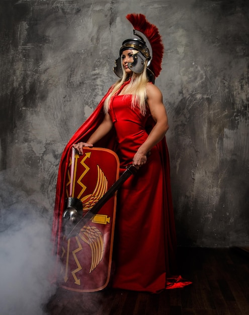 Roman warrior woman in red fluttering dress holds sword and shield.