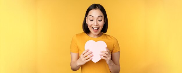 Romance and valentines day happy beautiful asian woman holding big heart card and smiling standing o