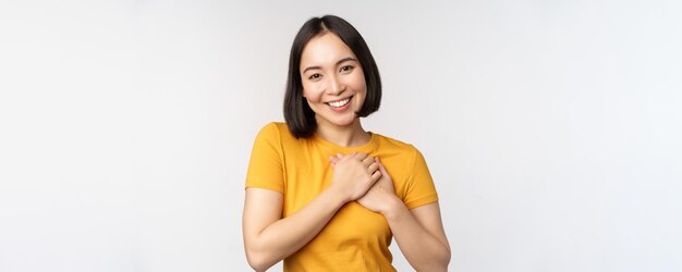 흰색 배경 위에 노란색 티셔츠를 입고 보살핌과 부드러움으로 웃고 있는 마음에 손을 잡고 있는 로맨틱한 아시아 여자친구