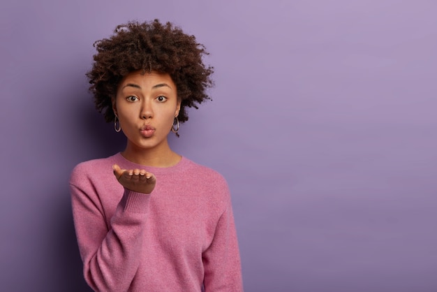 Free photo romantic beautiful woman with afro hair sends sensual air kiss from open palm