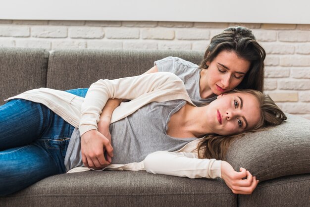 Romantic beautiful young lesbian couple lying on sofa