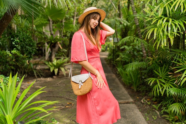 Romantic brunette woman in elegant pink dress enjoying tropical vacation