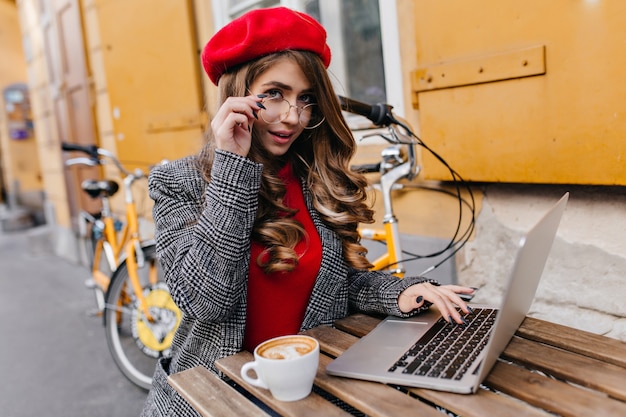 Foto gratuita businesslady romantica che lavora con il computer portatile mentre beve il caffè nella fredda giornata autunnale