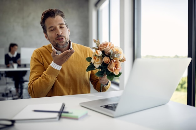 Romantic businessman sending a kiss during a video call over laptop in the office