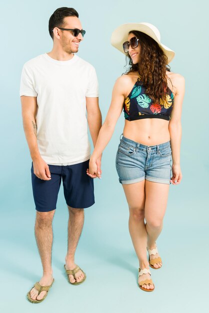 Romantic couple at the beach holding hands and looking at each other. Cute young woman and man going to the pool on a hot summer day