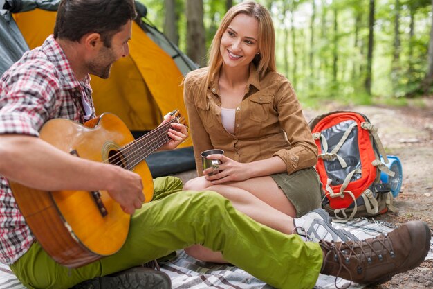 캠핑에서 로맨틱 커플입니다. 기타를 연주하는 남자.