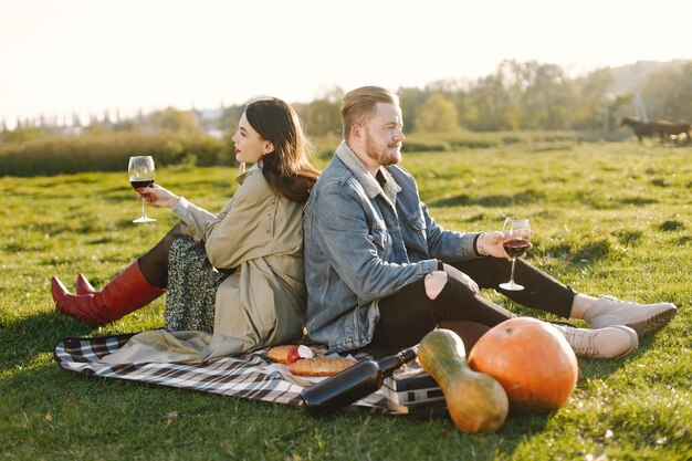 Romantic couple in fashion clothes sitting on a nature on a picnic rug. Man wearing jacket and woman coat