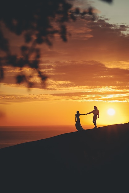 Romantic couple holding hands on the shore of the sea during sunset