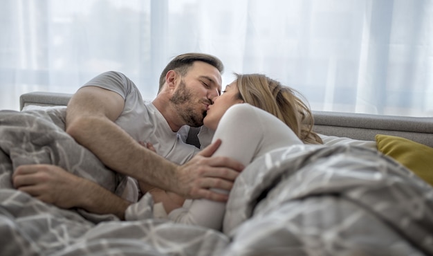 Romantic couple lying in the bed and embracing and kissing each other