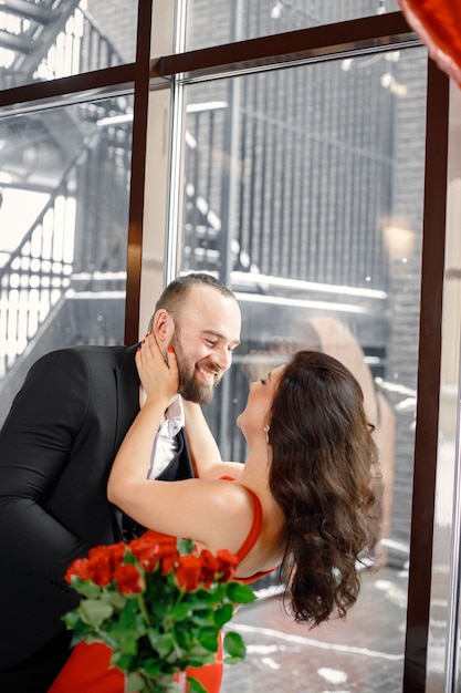 Free photo romantic couple standing in restaurant on a date near big window and hugging