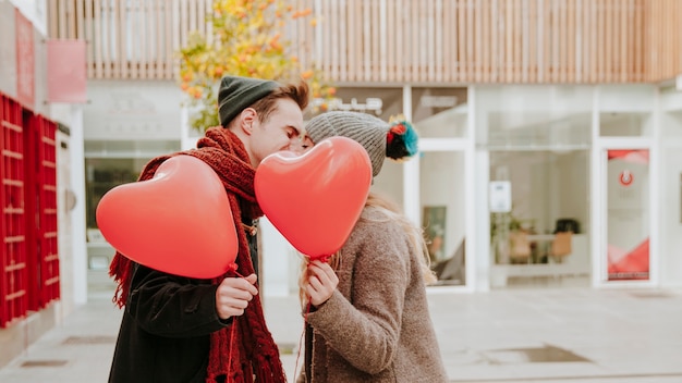 Romantic couple with balloons kissing on street