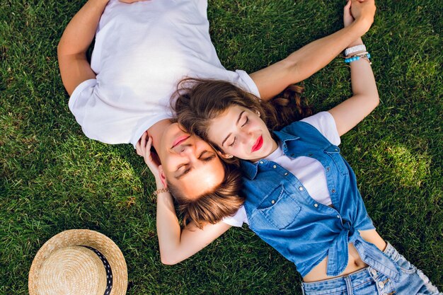 Романтическая пара молодых людей, лежа на траве в парке. Они лежат на плечах друг друга и держатся за руки. Они держат глаза закрытыми и выглядят расслабленными. Вид сверху.
