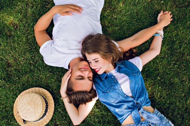 公園の芝生の上で横になっている若者のロマンチックなカップル。彼らはお互いの肩の上に横たわり、手をつないでいます。彼らは幸せそうに見えます。上からの眺め。