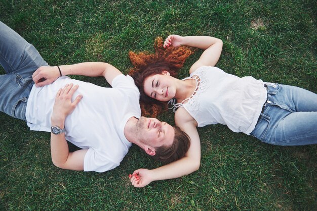 Romantic couple of young people lying on grass in park.