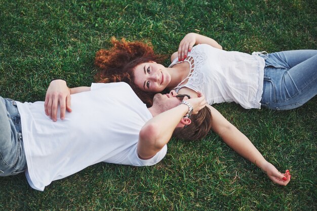 Romantic couple of young people lying on grass in park.