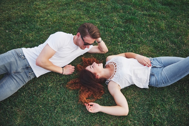 公園の芝生の上で横になっている若者のロマンチックなカップル。