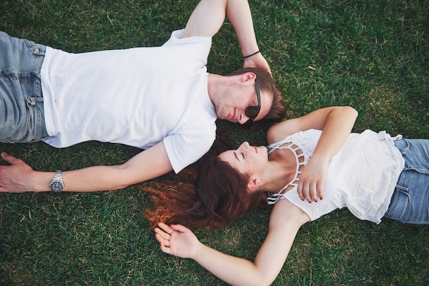 Romantic couple of young people lying on grass in park.