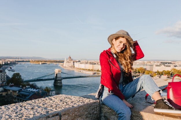 Romantic girl in black gumshoes sitting on roof and playing with brown hair