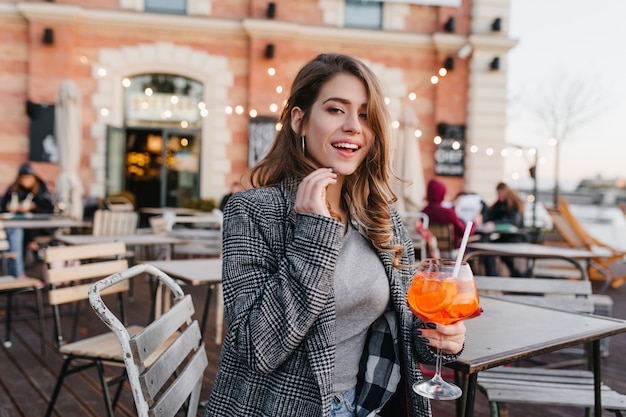 Romantic girl in casual clothes chilling in cafe in autumn weekend and tasting cocktail