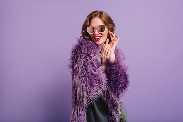 Romantic girl in stylish purple outfit posing with shy smile in studio