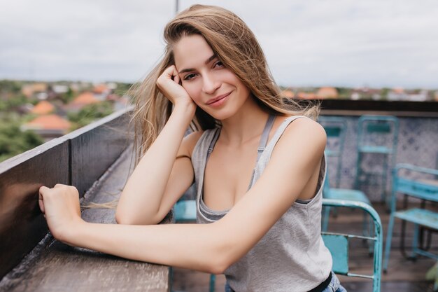 Romantic girl with pale skin sitting with gently smile. Outdoor photo of winsome young woman posing in roof cafe in good day.