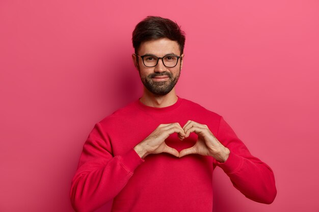 Romantic handsome bearded man makes heart shape symbol with fingers,