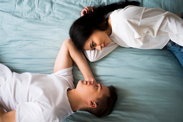 Free photo romantic loving couple lying on bed and looking into eyes