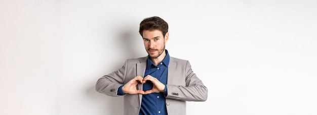 Romantic man in suit showing heart sign and smiling love his girlfriend standing on white background