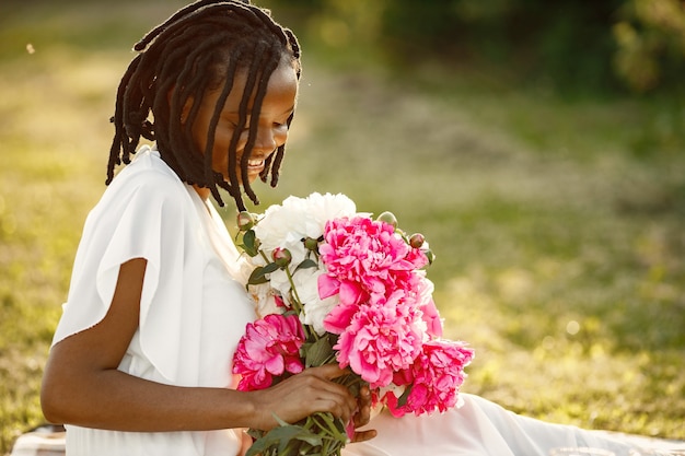 ロマンチックなピクニック。一人で座って花を嗅ぐ美しいアフリカ系アメリカ人の女性。夏時間。