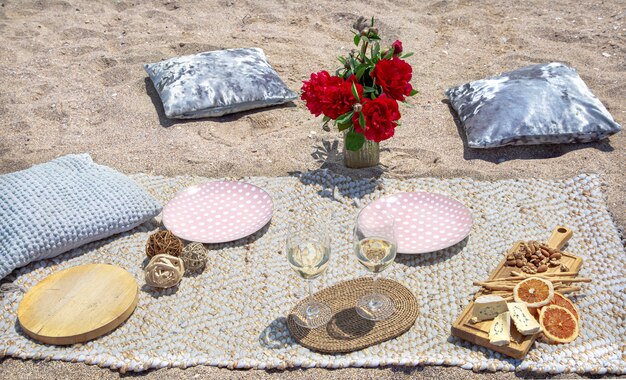 Romantic picnic on the sandy beach with champagne, snacks and flowers. Vacation and romance concept.