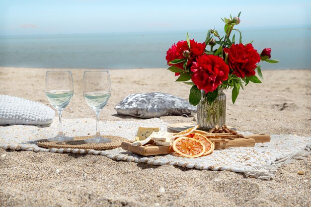 Романтический пикник на песчаном пляже с шампанским, закусками и цветами. Концепция отпуска и романтики.