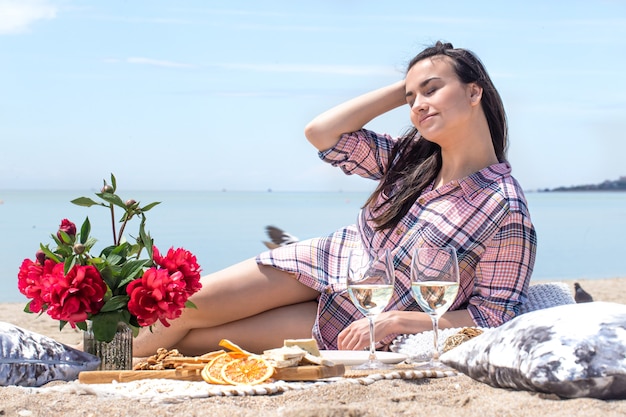 A romantic picnic on the sandy shore of the beach with flowers and glasses of drinks. The concept of summer vacation.